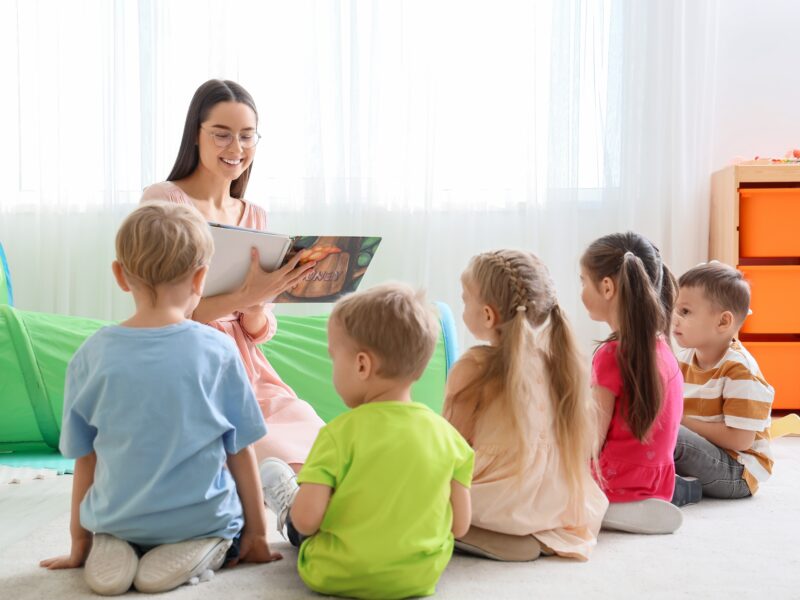 Nursery,Teacher,Reading,Story,To,Little,Children,In,Kindergarten