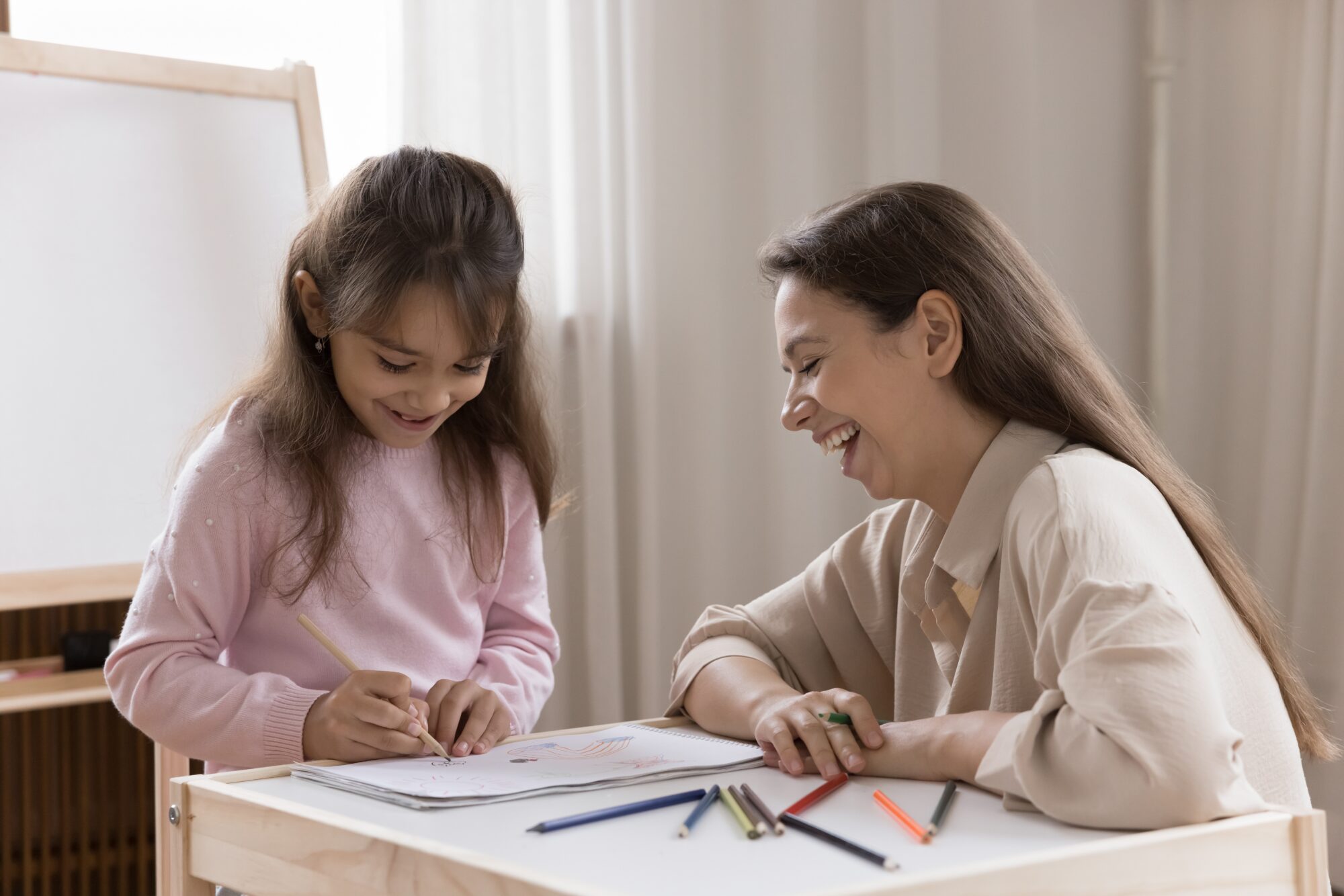 Joyful,Young,Mom,Older,Sister,Nanny,Sitting,At,Desk,Laughing